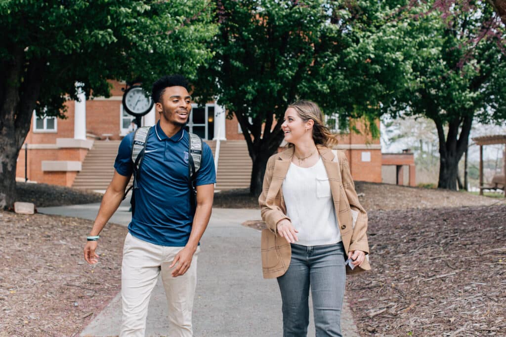 Two students talking and walking in front of the clock.