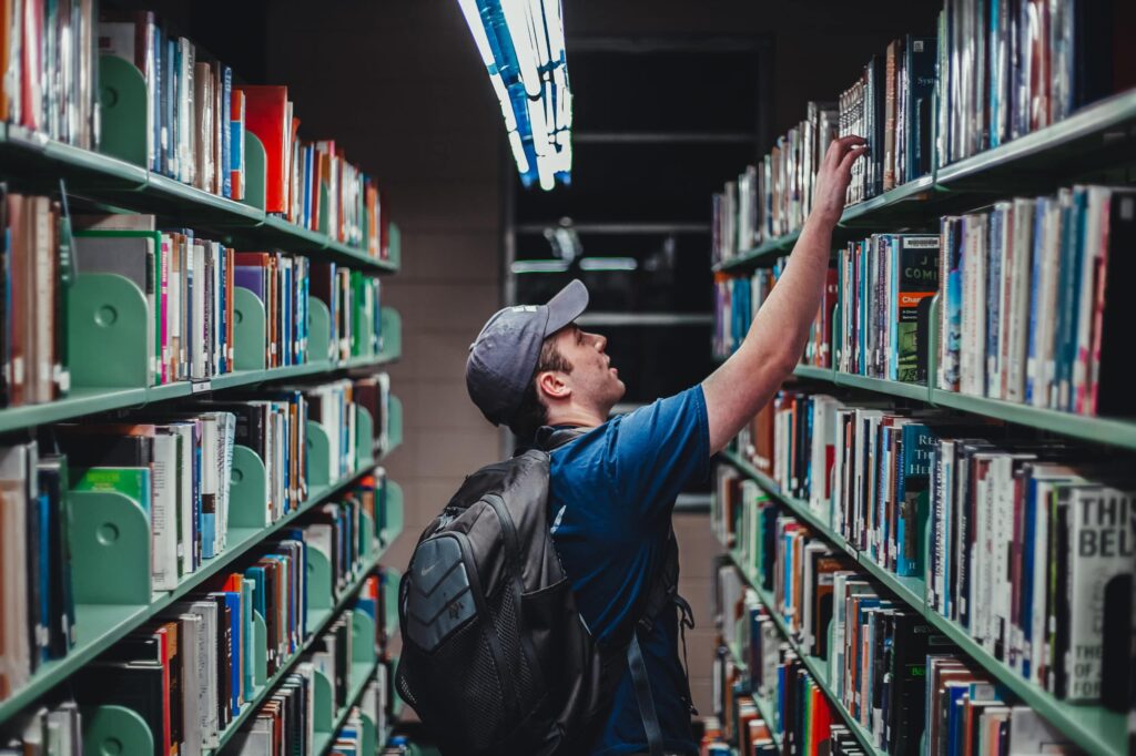 Man reaching for text book on a shelf