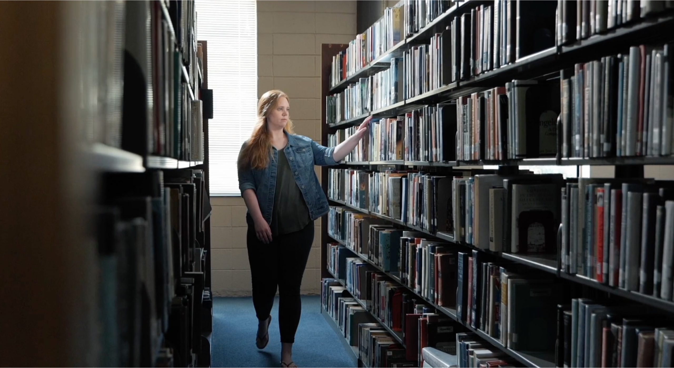 Young woman walking through library bookshelves